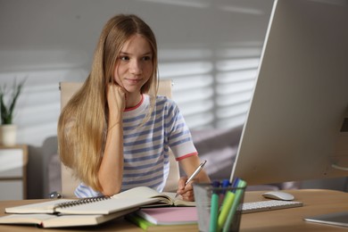 Photo of Teenage girl taking notes while studying online at table indoors