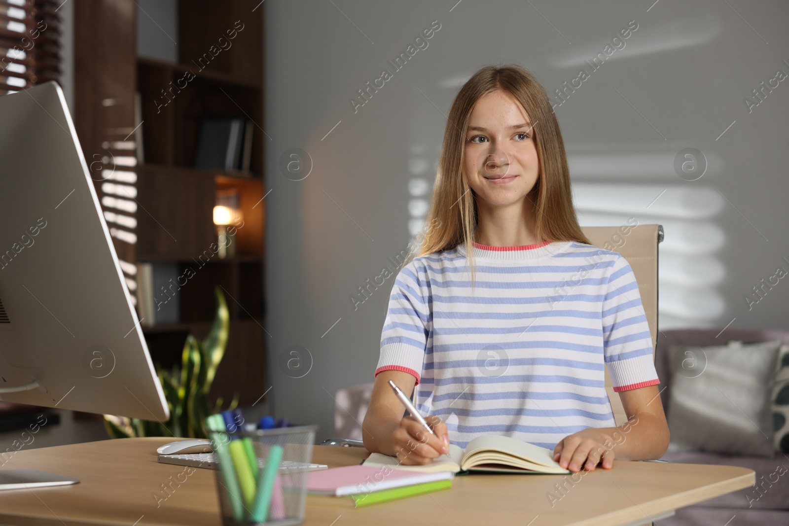 Teenage girl taking notes while studying online at table indoors Photo of Teenage girl taking notes while studying online at table indoors