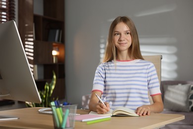 Photo of Teenage girl taking notes while studying online at table indoors