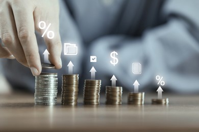 Image of Man stacking coins at wooden table, closeup. Arrows, percent signs and icons over stacks