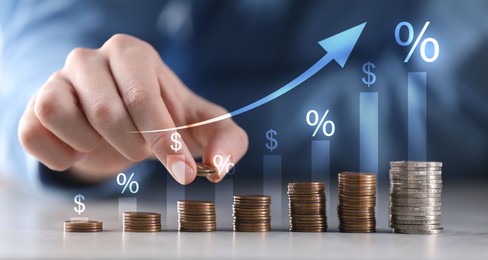 Image of Man stacking coins at table, closeup. Arrow, percent and dollar signs above stacks