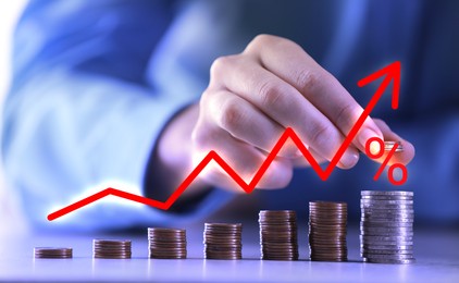 Image of Man stacking coins at table, closeup. Arrow and percent sign above stacks