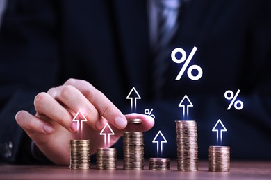 Image of Man stacking coins at table, closeup. Percent signs and arrows above stacks