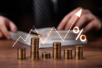 Image of Arrow and percent sign above stacked coins on wooden table. Man using calculator, selective focus