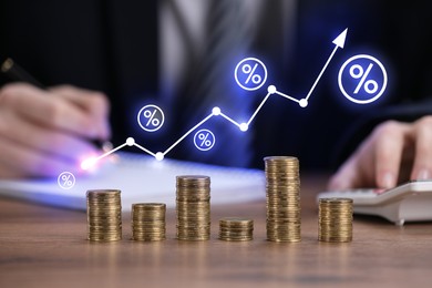 Image of Arrow and percent signs above stacked coins on wooden table. Man using calculator, selective focus