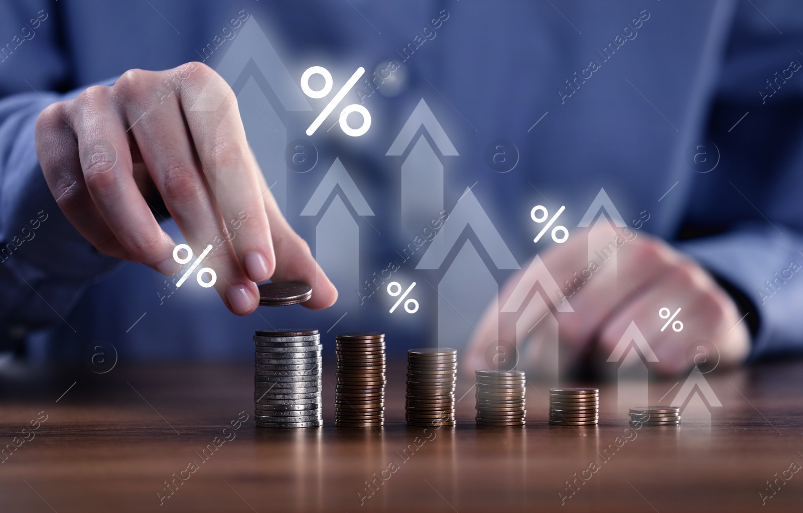 Image of Man stacking coins at wooden table, closeup. Percent signs and arrows above stacks