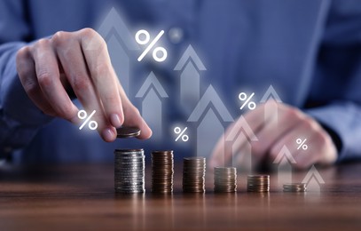 Image of Man stacking coins at wooden table, closeup. Percent signs and arrows above stacks