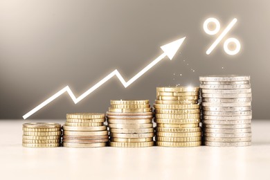 Image of Percent sign and arrow above stacked coins on table against grey background