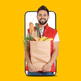 Image of Delivery service worker giving online order out of mobile phone against orange background. Man with paper bag full of food products