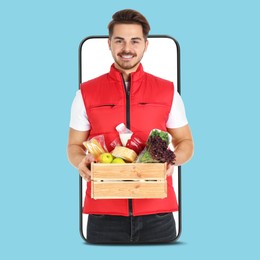 Image of Delivery service worker giving order out of mobile phone against light blue background. Man with crate full of food products