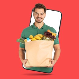 Image of Delivery service worker giving order out of mobile phone against red background. Man with paper bag full of food products