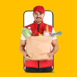 Image of Delivery service worker giving online order out of mobile phone against orange background. Man with paper bag full of food products