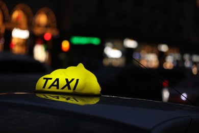 Photo of Taxi car with yellow checkered sign on city street in evening, closeup
