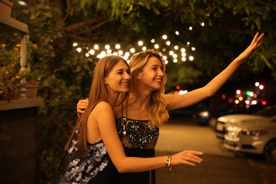 Photo of Young women catching taxi on city street at night