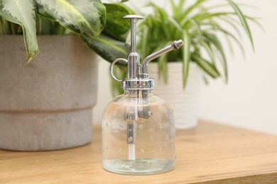 Photo of Spray bottle and different houseplants on wooden table indoors, closeup