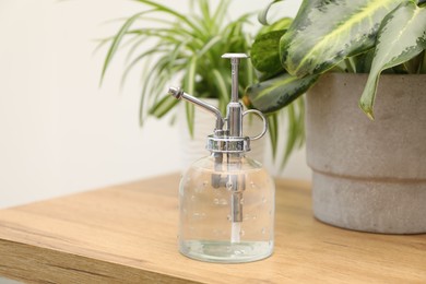 Photo of Spray bottle and different houseplants on wooden table indoors, closeup