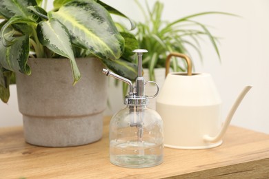 Photo of Spray bottle, watering can and different houseplants on wooden table indoors, closeup