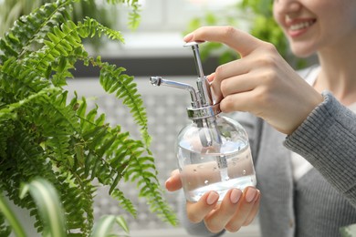 Photo of Young woman spraying beautiful houseplant with water from bottle indoors, closeup