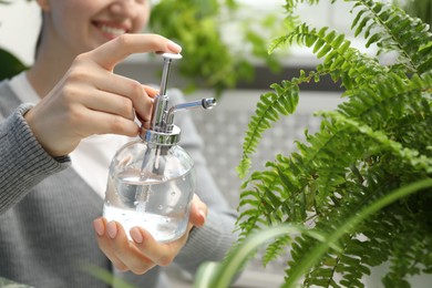 Photo of Young woman spraying beautiful houseplant with water from bottle indoors, closeup