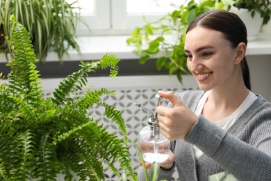 Photo of Young woman spraying beautiful houseplant with water from bottle indoors