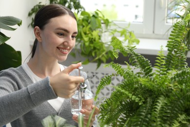 Photo of Young woman spraying beautiful houseplant with water from bottle indoors