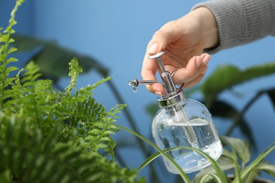 Photo of Young woman spraying beautiful houseplant with water from bottle indoors, closeup