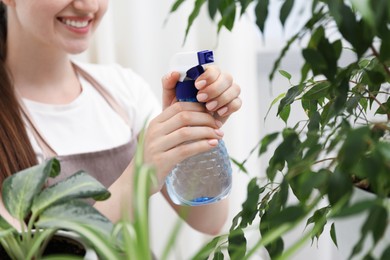Photo of Young woman spraying beautiful houseplant with water from bottle indoors, closeup