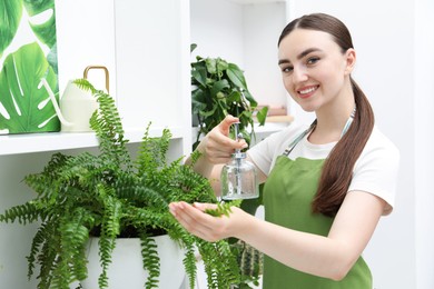 Photo of Young woman spraying beautiful houseplant with water from bottle indoors