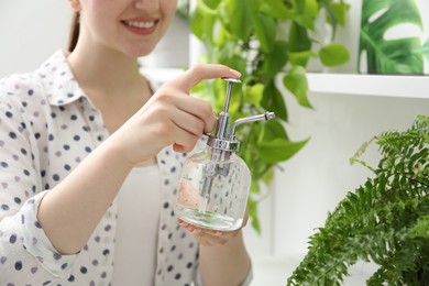 Photo of Young woman spraying beautiful houseplant with water from bottle indoors, closeup