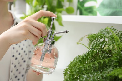 Photo of Young woman spraying beautiful houseplant with water from bottle indoors, closeup