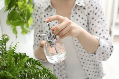 Photo of Young woman spraying beautiful houseplant with water from bottle indoors, closeup