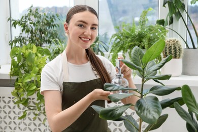 Photo of Young woman spraying beautiful houseplant with water from bottle indoors