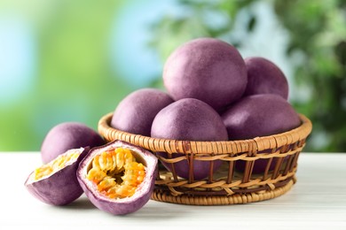 Photo of Fresh passion fruits in wicker basket on white wooden table outdoors, closeup