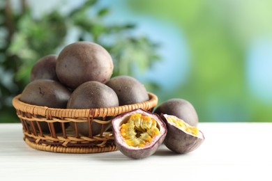 Photo of Fresh passion fruits in wicker basket on white wooden table outdoors, space for text