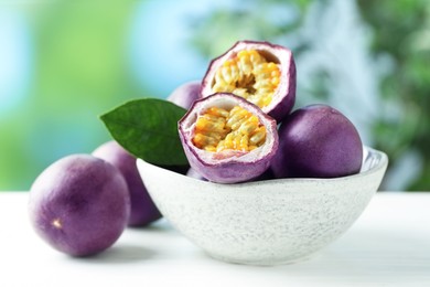 Photo of Fresh passion fruits in bowl on white wooden table outdoors, closeup