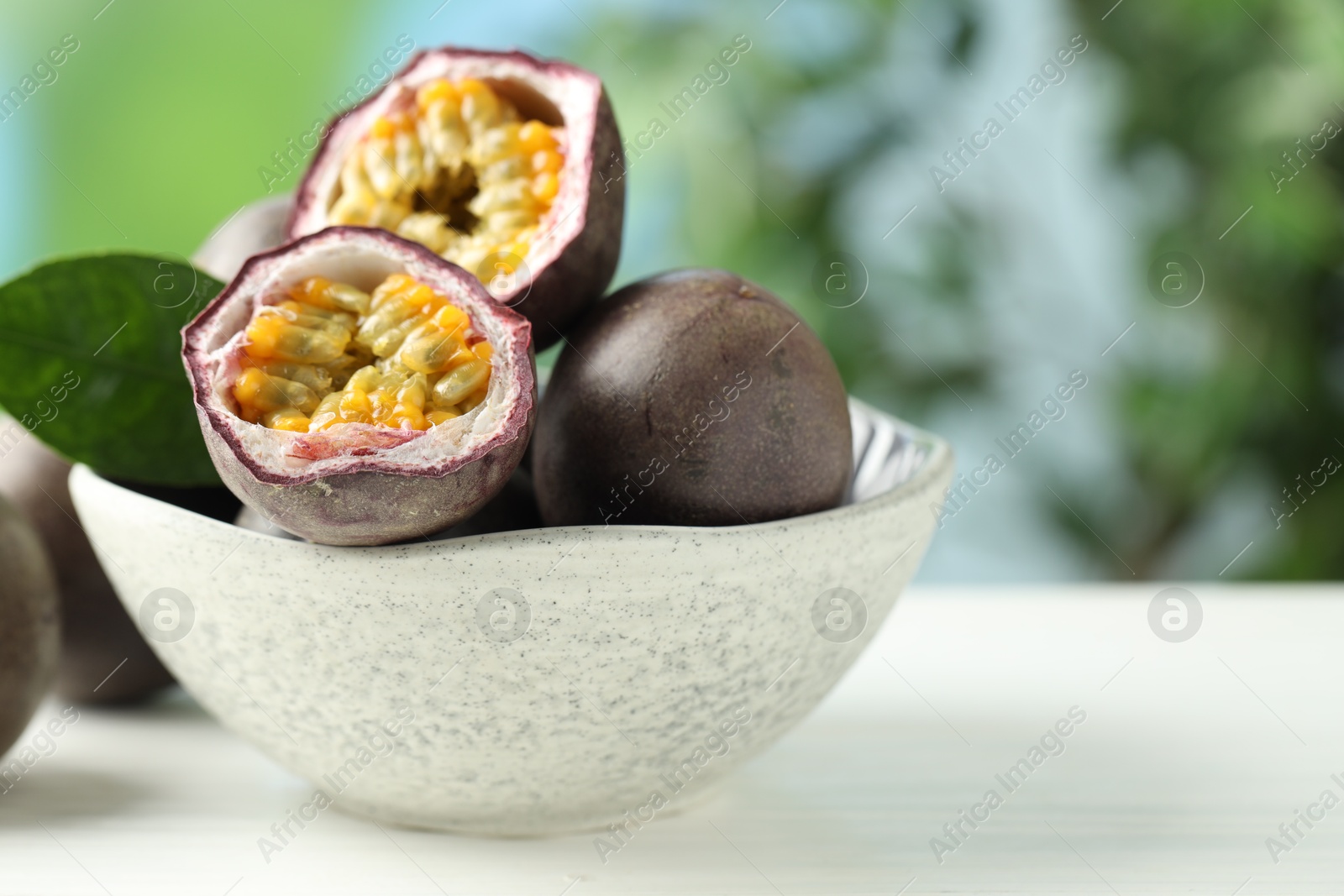 Fresh passion fruits in bowl on white wooden table outdoors, closeup. Space for text Photo of Fresh passion fruits in bowl on white wooden table outdoors, closeup. Space for text