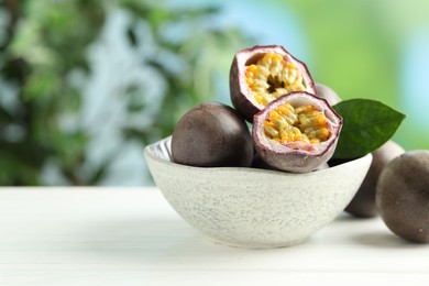 Photo of Fresh passion fruits in bowl on white wooden table outdoors, closeup. Space for text