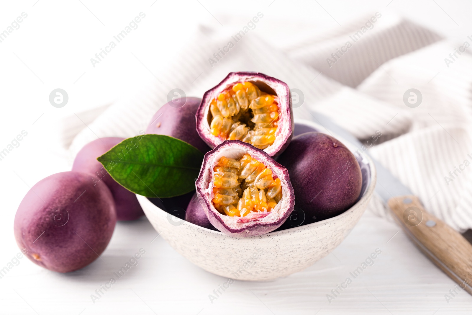 Fresh passion fruits in bowl and knife on white wooden table, closeup Photo of Fresh passion fruits in bowl and knife on white wooden table, closeup