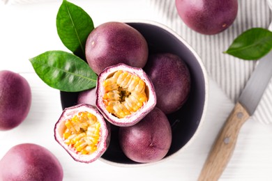 Photo of Fresh passion fruits in bowl and knife on white wooden table, flat lay