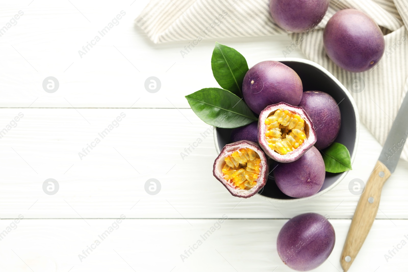 Fresh passion fruits in bowl, leaves and knife on white wooden table, flat lay. Space for text Photo of Fresh passion fruits in bowl, leaves and knife on white wooden table, flat lay. Space for text