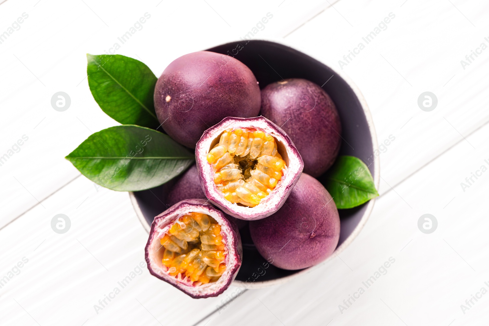 Fresh passion fruits and green leaves in bowl on white wooden table, top view Photo of Fresh passion fruits and green leaves in bowl on white wooden table, top view