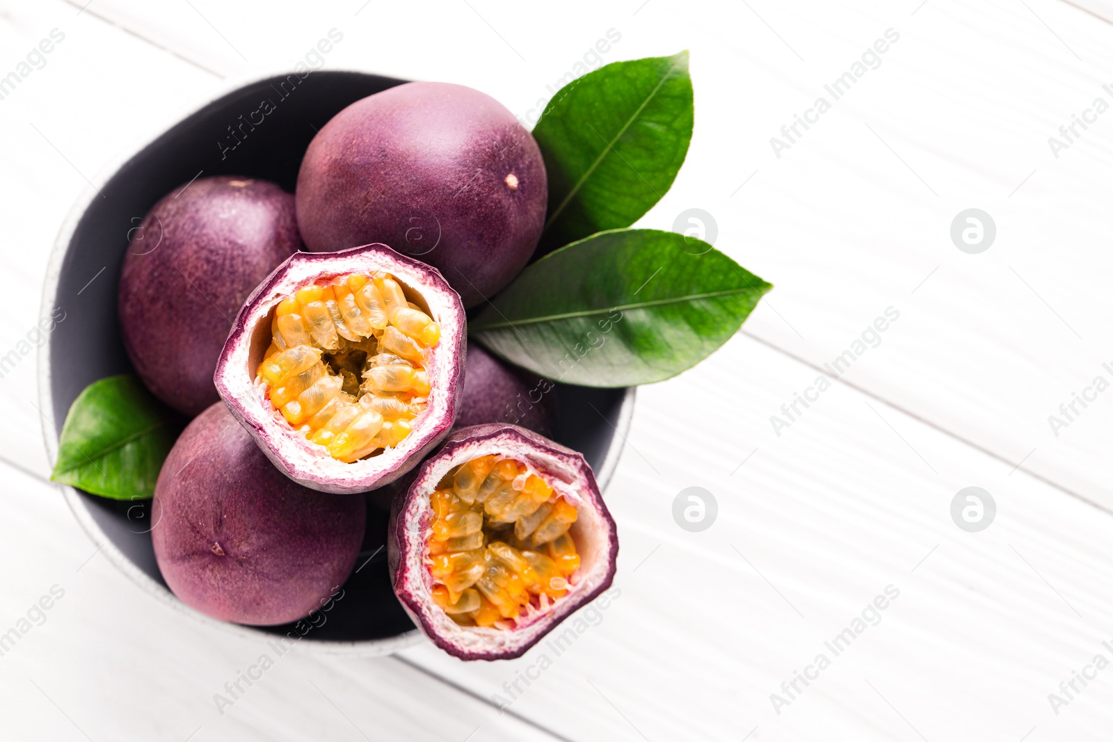 Fresh passion fruits and green leaves in bowl on white wooden table, top view. Space for text Photo of Fresh passion fruits and green leaves in bowl on white wooden table, top view. Space for text
