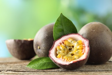 Photo of Fresh passion fruits and green leaves on wooden table outdoors, closeup