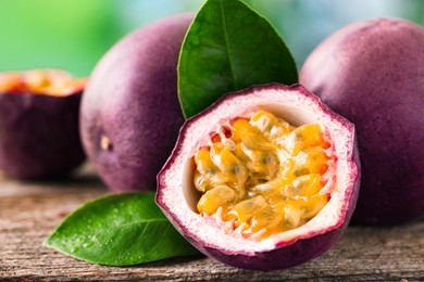 Photo of Fresh passion fruits and green leaves on wooden table outdoors, closeup