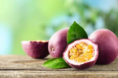 Photo of Fresh passion fruits and green leaves on wooden table outdoors, closeup. Space for text