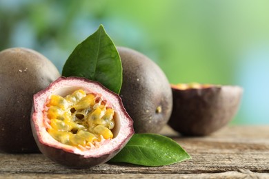 Photo of Fresh passion fruits and green leaves on wooden table outdoors, closeup. Space for text