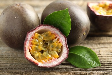 Photo of Fresh passion fruits and green leaves on wooden table, closeup