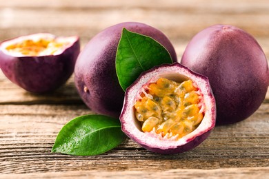 Photo of Fresh passion fruits and green leaves on wooden table, closeup