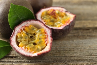 Photo of Fresh passion fruits and green leaves on wooden table, closeup. Space for text