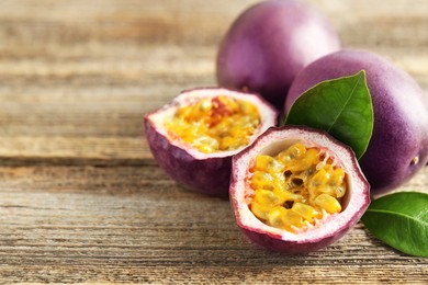 Photo of Fresh passion fruits and green leaves on wooden table, closeup. Space for text